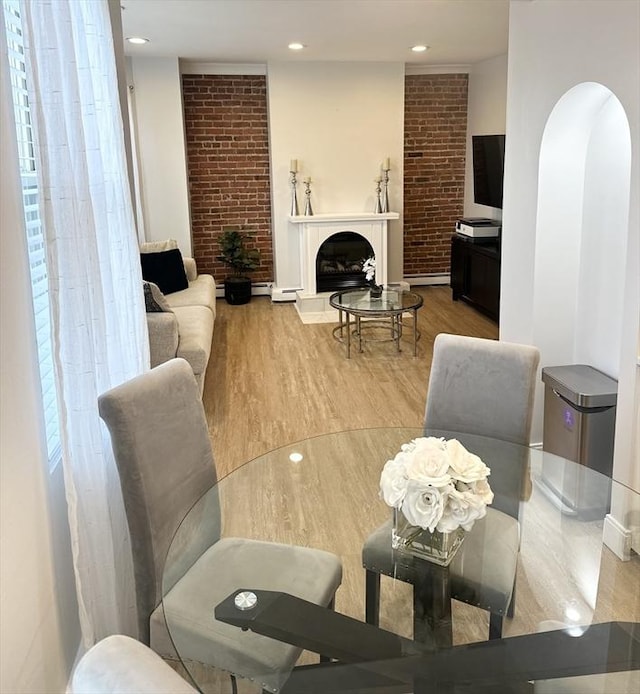 living room with light wood-type flooring, brick wall, and a baseboard heating unit