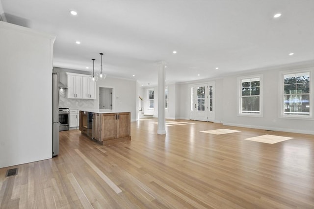 unfurnished living room with light wood-type flooring, ornamental molding, and decorative columns