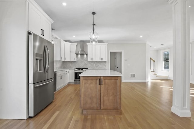 kitchen featuring appliances with stainless steel finishes, wall chimney exhaust hood, a kitchen island, white cabinetry, and hanging light fixtures