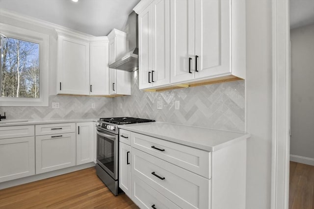 kitchen with white cabinetry, stainless steel range with gas cooktop, wall chimney range hood, and light hardwood / wood-style flooring