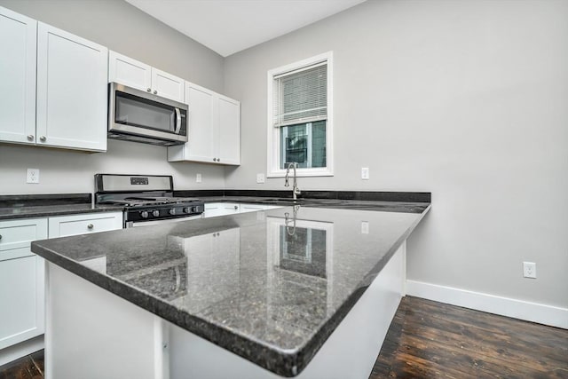 kitchen featuring sink, dark hardwood / wood-style flooring, white cabinetry, stainless steel appliances, and dark stone counters