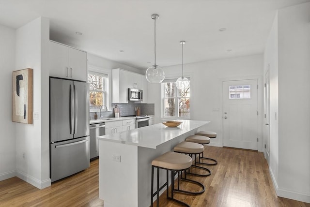 kitchen featuring appliances with stainless steel finishes, tasteful backsplash, pendant lighting, white cabinets, and a center island