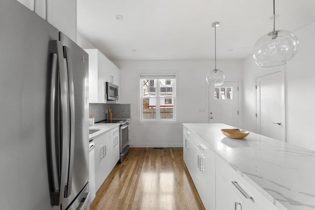 kitchen featuring decorative backsplash, white cabinetry, pendant lighting, and appliances with stainless steel finishes