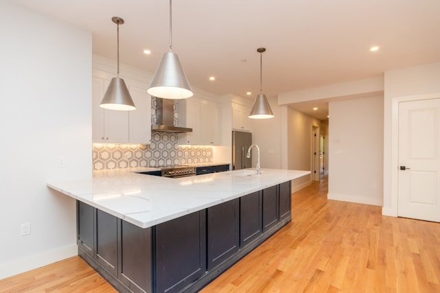 kitchen featuring wall chimney range hood, light wood-type flooring, backsplash, and white cabinetry