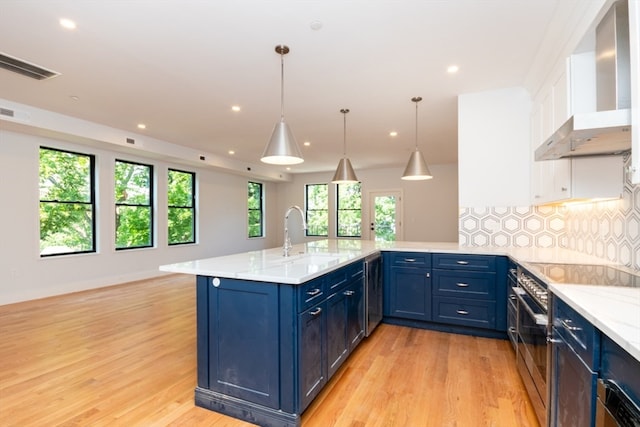 kitchen featuring wall chimney range hood, light hardwood / wood-style flooring, tasteful backsplash, plenty of natural light, and decorative light fixtures