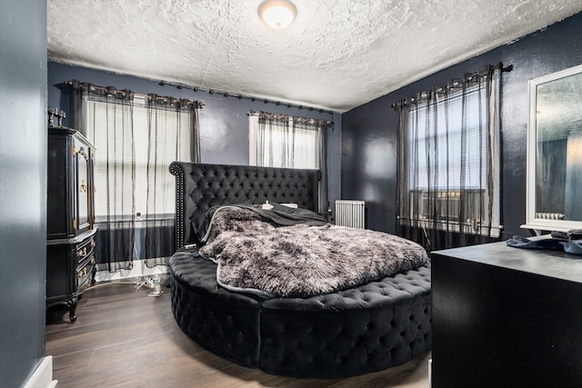 bedroom featuring a textured ceiling, radiator, multiple windows, and hardwood / wood-style flooring