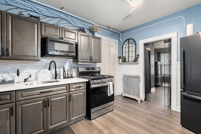 kitchen featuring black appliances, light hardwood / wood-style floors, tasteful backsplash, and sink