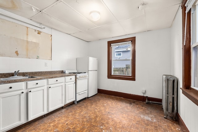 kitchen featuring white appliances, radiator, sink, white cabinets, and a drop ceiling