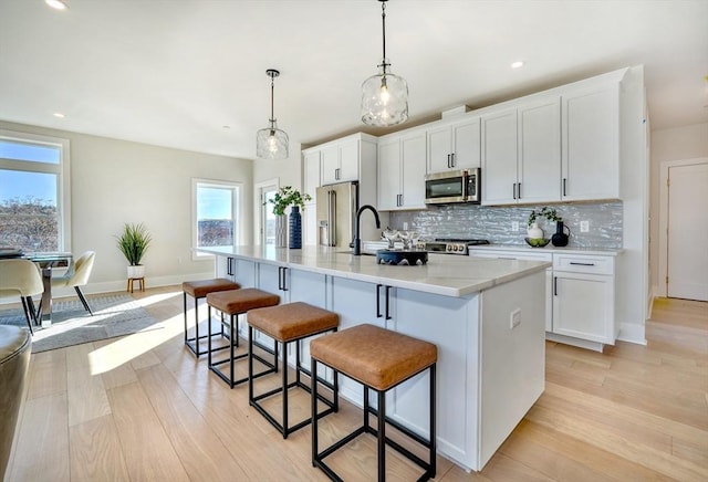 kitchen with white cabinetry, appliances with stainless steel finishes, a kitchen island with sink, and hanging light fixtures