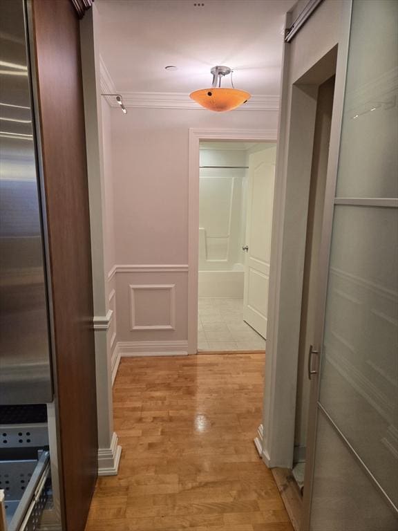 hall with a decorative wall, light wood-type flooring, ornamental molding, and a wainscoted wall