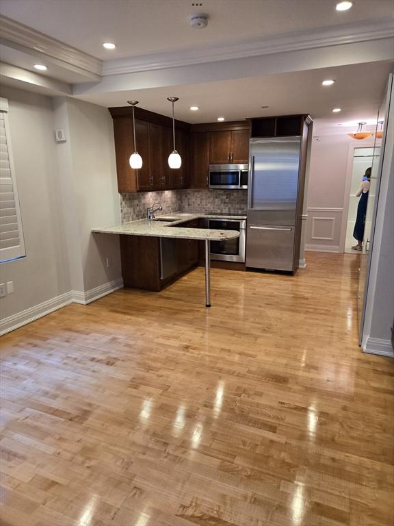 kitchen featuring tasteful backsplash, dark brown cabinetry, light wood-type flooring, appliances with stainless steel finishes, and a sink