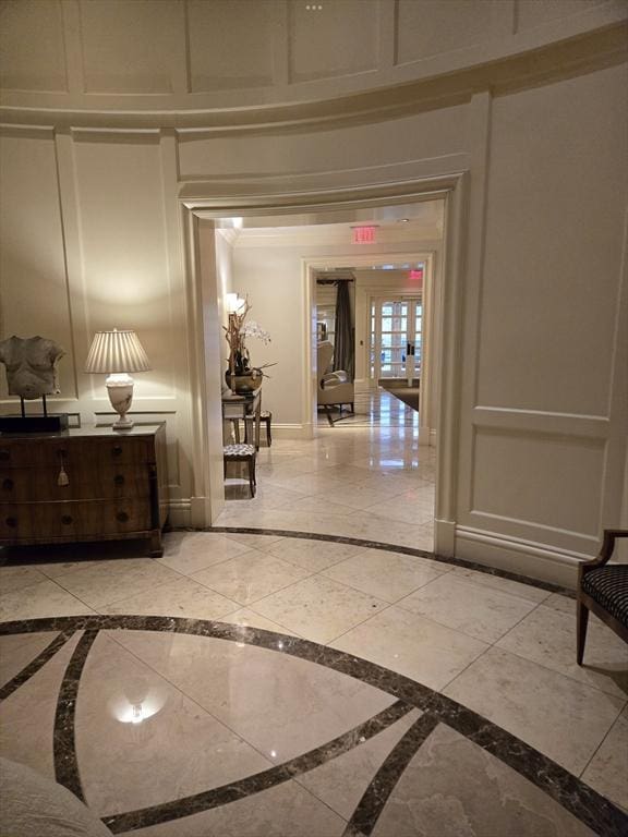 hallway featuring a decorative wall, marble finish floor, baseboards, and ornamental molding
