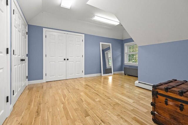 bedroom with baseboard heating, lofted ceiling, light hardwood / wood-style flooring, and two closets