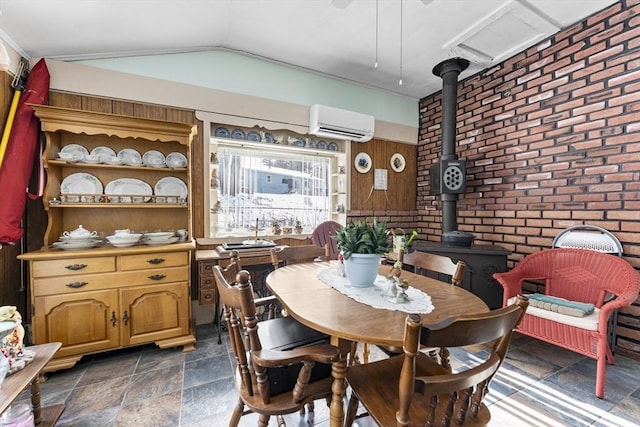 dining room with a wall unit AC, lofted ceiling, a wood stove, stone finish floor, and brick wall