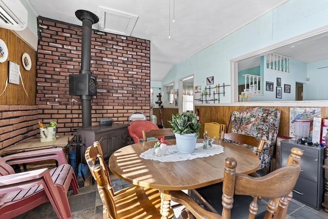 dining space with a wood stove, a wall unit AC, and vaulted ceiling