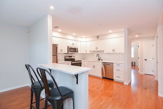 kitchen featuring white cabinetry, backsplash, stainless steel appliances, light hardwood / wood-style flooring, and sink