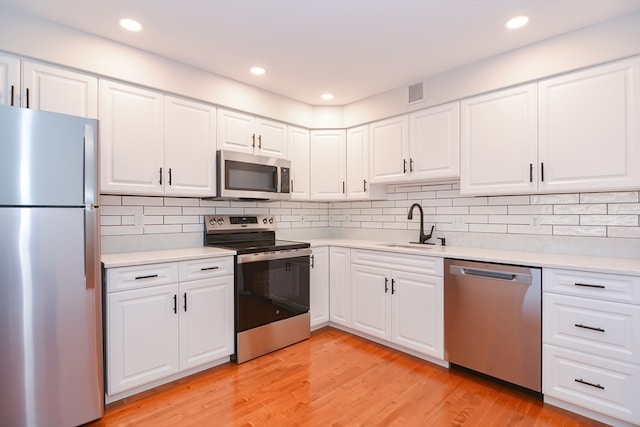 kitchen featuring appliances with stainless steel finishes, decorative backsplash, white cabinetry, light wood-type flooring, and sink