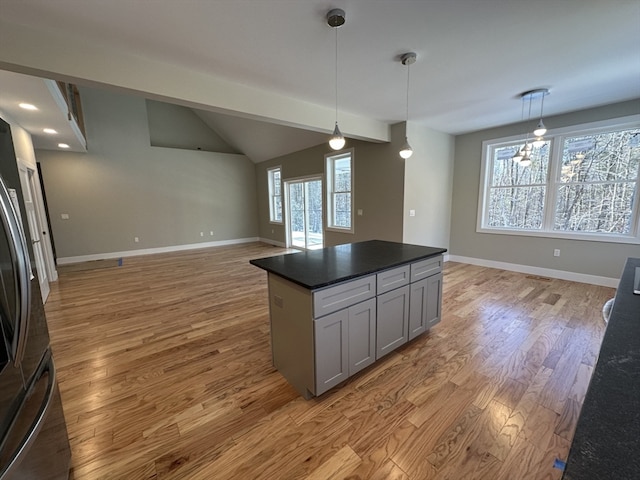 kitchen with gray cabinetry, vaulted ceiling, decorative light fixtures, a center island, and light hardwood / wood-style floors