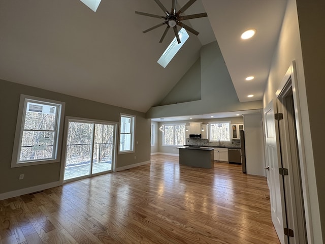 unfurnished living room with hardwood / wood-style floors, a skylight, high vaulted ceiling, and ceiling fan