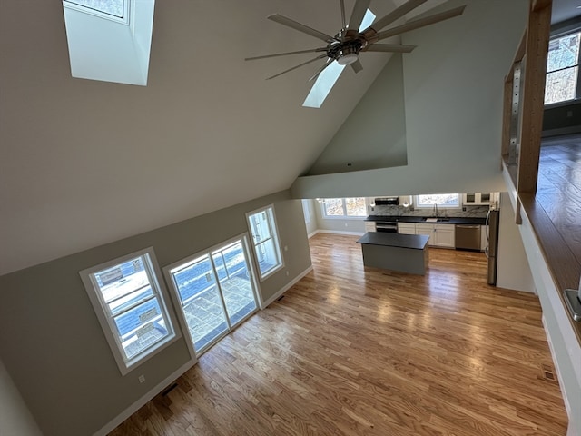 unfurnished living room featuring hardwood / wood-style floors, a skylight, high vaulted ceiling, and sink