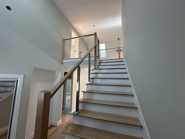 staircase featuring hardwood / wood-style flooring, ceiling fan, and a towering ceiling