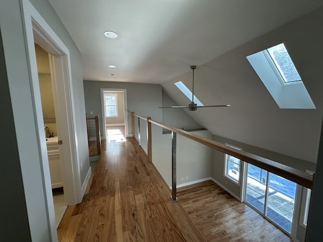 hallway with vaulted ceiling with skylight and light wood-type flooring