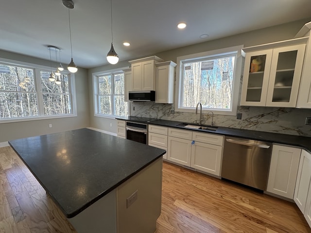 kitchen with sink, a center island, hanging light fixtures, stainless steel appliances, and light hardwood / wood-style flooring