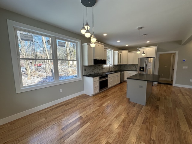 kitchen with appliances with stainless steel finishes, white cabinets, light hardwood / wood-style floors, a kitchen island, and hanging light fixtures