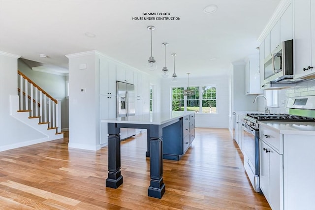 kitchen featuring stainless steel appliances, pendant lighting, white cabinets, light hardwood / wood-style floors, and a kitchen island