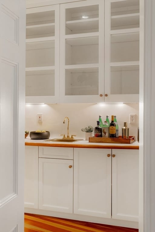 bar with light wood-type flooring, white cabinetry, and sink