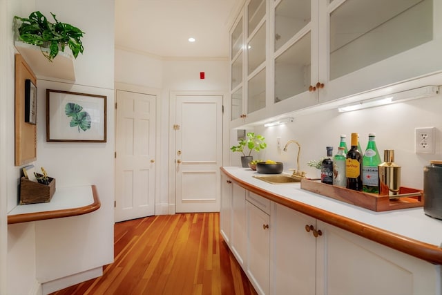 bar featuring ornamental molding, sink, light hardwood / wood-style flooring, and white cabinets