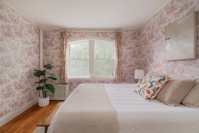 bedroom with radiator heating unit, hardwood / wood-style flooring, and ornamental molding