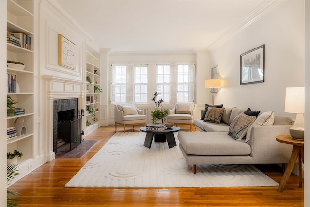 living room with a tile fireplace, ornamental molding, built in features, and hardwood / wood-style flooring