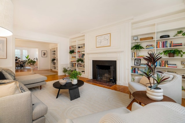 living room with crown molding, built in shelves, and light hardwood / wood-style flooring