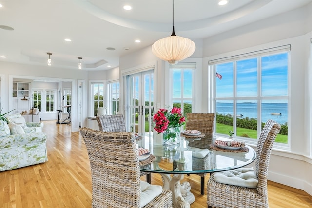 dining space with a water view, a tray ceiling, and light wood-type flooring