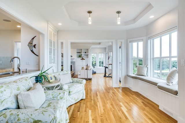 living room featuring light wood-type flooring, a fireplace, a tray ceiling, and sink