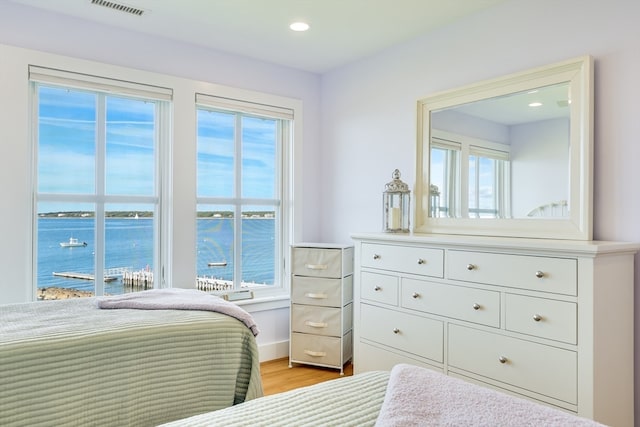 bedroom with light hardwood / wood-style flooring, multiple windows, and a water view