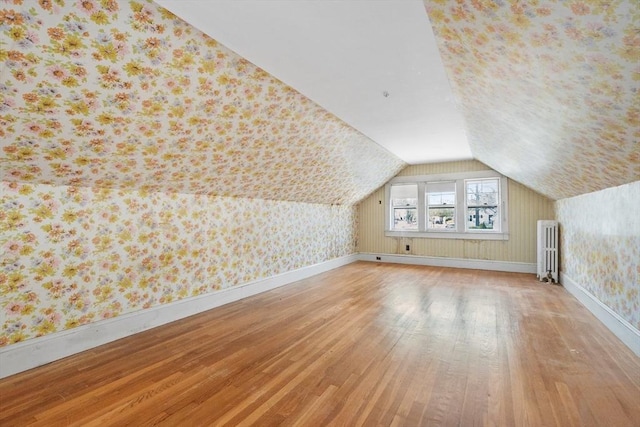 additional living space with radiator, wood finished floors, vaulted ceiling, and wallpapered walls