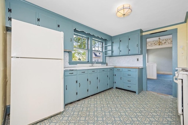 kitchen with decorative backsplash, blue cabinetry, open shelves, light countertops, and freestanding refrigerator
