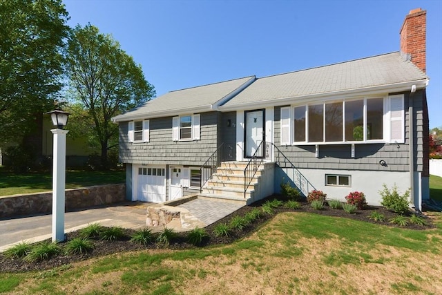 single story home featuring a garage, a front lawn, a chimney, and driveway