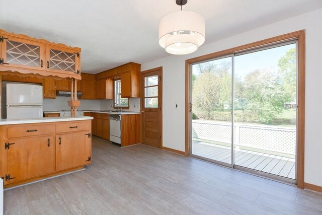 kitchen with white appliances, under cabinet range hood, light countertops, hanging light fixtures, and baseboards