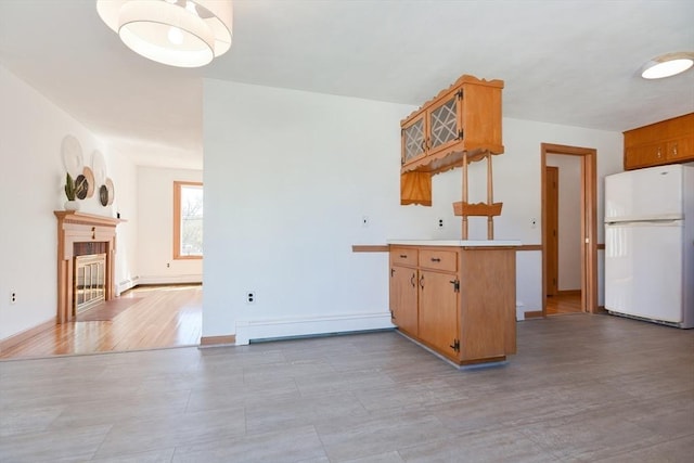 kitchen featuring freestanding refrigerator, a baseboard heating unit, a peninsula, a tile fireplace, and light countertops