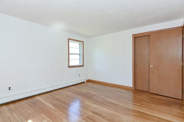 unfurnished bedroom featuring a closet, baseboards, light wood-style flooring, and a baseboard radiator