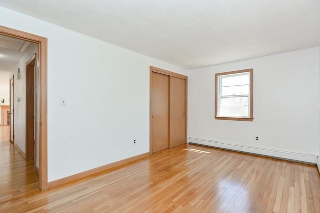 spare room featuring attic access, light wood-style floors, baseboards, and a baseboard radiator