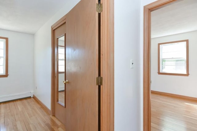 hallway with a baseboard heating unit, baseboards, a healthy amount of sunlight, and light wood-type flooring