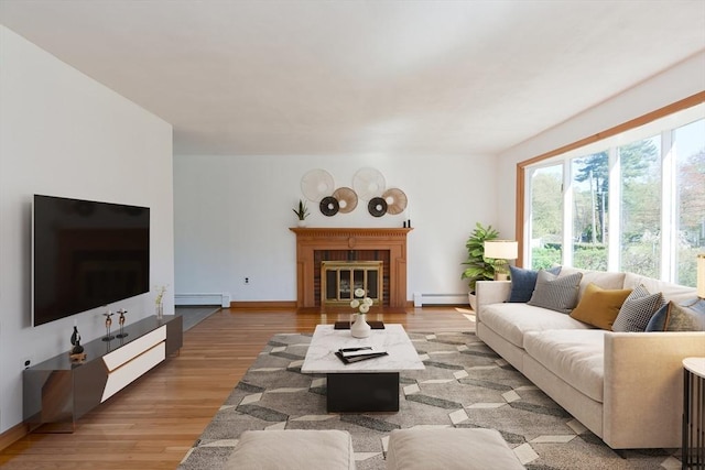 living room featuring light wood-style floors, baseboards, baseboard heating, and a glass covered fireplace
