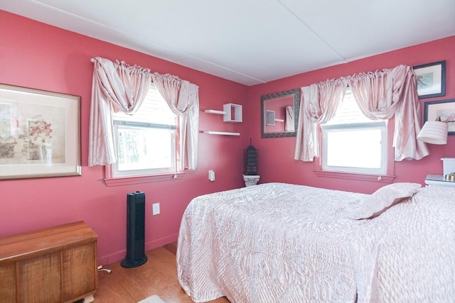 bedroom with multiple windows, baseboards, and wood finished floors