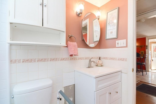 half bath featuring tile walls, wainscoting, vanity, and toilet