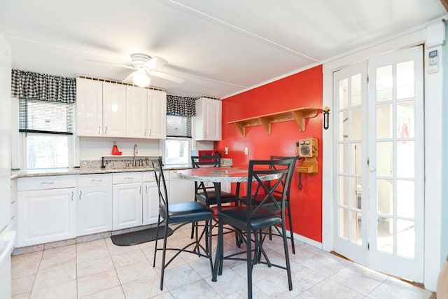 kitchen with light tile patterned floors, white cabinets, ceiling fan, light stone counters, and a sink