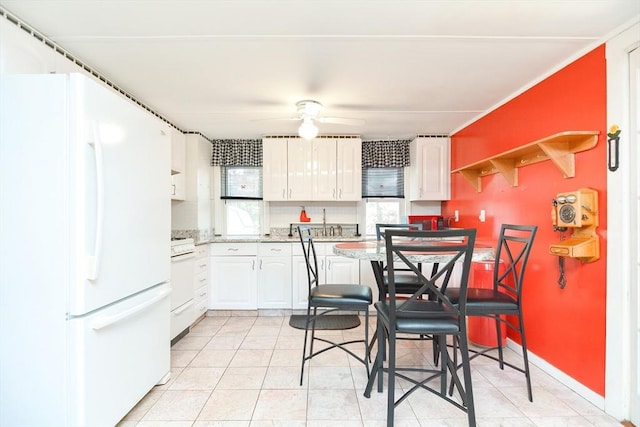 kitchen featuring light tile patterned floors, freestanding refrigerator, white cabinetry, ceiling fan, and range